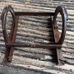 May include: A rustic metal stand made from two horseshoes and metal bars. The stand is weathered and has a brown patina.