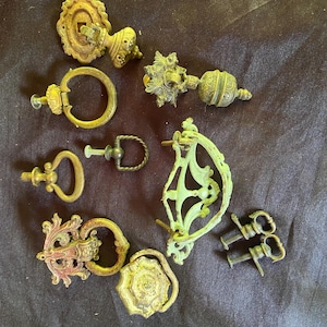 Könnte beinhalten: Sortiment an antiken Schrankbeschlägen, darunter verzierte Griffe, Knöpfe und Scharniere. Die Beschläge sind aus Metall und haben verschiedene Oberflächen, darunter Messing, Bronze und Silber.
