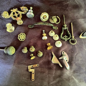 Könnte beinhalten: Eine Auswahl an antiken Schrankknöpfen und -griffen in verschiedenen Stilen und Ausführungen, darunter Messing, Silber und Porzellan. Einige haben verzierte Designs, während andere schlicht und funktional sind. Diese Beschläge wären perfekt, um jedem Einrichtungsprojekt einen Hauch von Vintage-Charme zu verleihen.