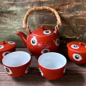 Może przedstawiać: Biały ceramiczny kubek z czarnym uchwytem i napisem "But First, Coffee" czarną, odręczną czcionką. Kubek stoi na białej powierzchni.