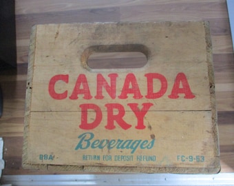 May include: Vintage wooden crate for Canada Dry Beverages. The crate is brown with red and green lettering. The text on the crate reads "Canada Dry Beverages" and "Return for Deposit Refund". The date "FC-9-53" is printed on the bottom right corner of the crate.