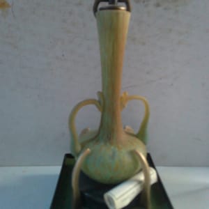 May include: A green and brown ceramic bottle with a gold metal stopper and a scroll on a black base. The base has a label that reads "Roman Wine Vessel 1st-4th Century A.D."