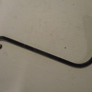 May include: A black, wrought iron plant hanger with a curled end and a right-angled hook. The hanger is designed to hold a hanging basket or other decorative items. The metal has a slightly textured surface.