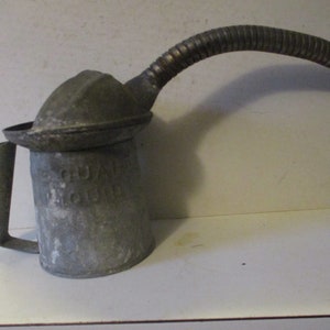 May include: A vintage metal oil can with a long spout and a handle. The can is gray and has the words "Quaker State Oil" printed on the side.
