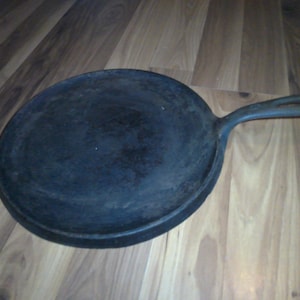May include: A black cast iron pan with a long handle. The pan is slightly dirty and has a rustic look.