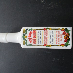 May include: White ceramic bottle shaped like a bottle of salad dressing with a green and yellow floral design and red text that reads "My Own Salad Dressing". The text on the bottle reads "Prepared from an old secret family recipe. Guaranteed to contain only the finest ingredients. Not available at the finest food shops. Note recipe given free to friends and guests on request."