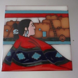 May include: Square ceramic tile featuring a Native American woman in profile, wearing a red shawl and blue earrings. The background depicts adobe buildings and a colorful sky. The tile has a glossy finish.