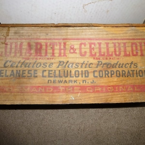 May include: A wooden box with a red and black label that reads "CUMARITH & CELLULOID Reg. U.S. Pat. Off. Cellulose Plastic Products CELANESE CELLULOID CORPORATION NEWARK, N.J. IN DEMAND THE ORIGINAL".