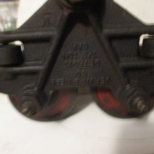 May include: Close-up of a black metal pulley system with two red wheels. The pulley has text that reads "DETROIT" and "STEEL STROKE". The wheels are approximately 3 inches in diameter.