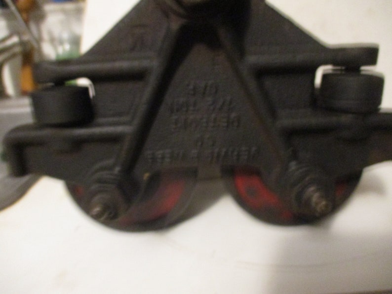 May include: Close-up of a black metal pulley system with two red wheels. The pulley has text that reads "DETROIT" and "STEEL STROKE". The wheels are approximately 3 inches in diameter.
