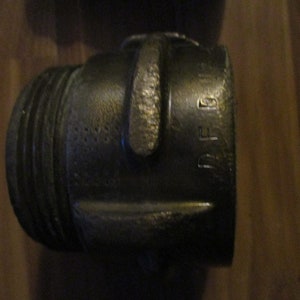 May include: Close-up of a dark metal fitting with a threaded end and a textured surface. The fitting has a handle and the letters "PF 16" are visible on the side. The object appears to be a plumbing or industrial component.