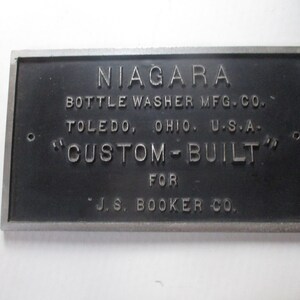 May include: A black metal plaque with silver lettering that reads "NIAGARA BOTTLE WASHER MFG. CO. TOLEDO, OHIO U.S.A. "CUSTOM-BUILT" FOR J.S. BOOKER CO."