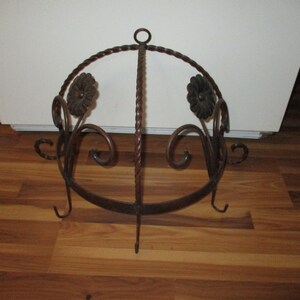 May include: A wrought iron pot rack with a twisted design and floral accents. The rack has three hooks on the bottom and a ring at the top for hanging.