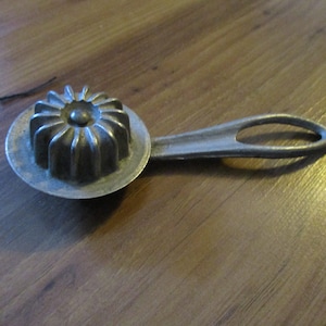 May include: A vintage metal cake mold with a starburst design and a long handle. The mold is silver in color and has a smooth surface.