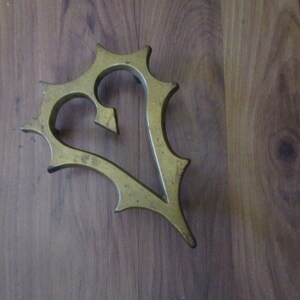 May include: A gold-colored, heart-shaped decorative object with a spiky, ornate border. The heart has a pointed arrow-like element at the top. The object is placed on a wooden surface.