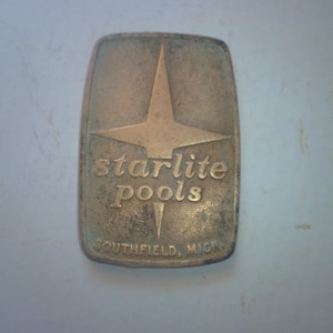 May include: A gold-colored metal plaque with a five-pointed star and the text "starlite Pools SOUTHFIELD, MICH."