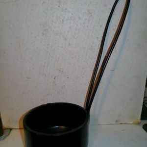 May include: A black ladle with a long, curved handle. The ladle's bowl is round and deep, and the handle is made of a dark, possibly metal material. The handle is attached to the bowl with a loop.