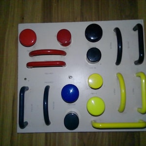 May include: A white board with various colored knobs and handles. The knobs are red, blue, yellow, and black. The handles are black, red, and yellow. The board is labeled with the words "PRO-RED", "PRO-BL", "PRO-Y", and "PRO-RED".