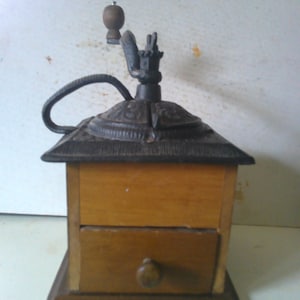 May include: Antique cast iron coffee grinder with a wooden base and drawer. The grinder has a crank handle and a hopper for coffee beans.