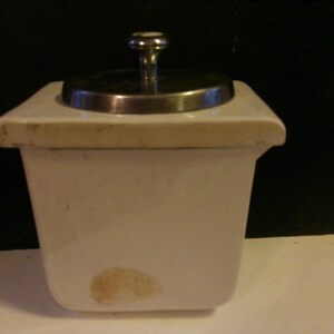 May include: White ceramic sugar bowl with a silver lid and knob. The bowl has a round, slightly raised rim and a smooth, white finish.