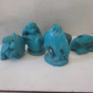 May include: A collection of turquoise-colored animal figurines, including a turtle, monkey, camel, and a creature with a hole. The figurines are likely made of a solid material and are displayed against a plain background.