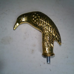 May include: A golden-colored bird-shaped handle, likely for a cane or walking stick. The handle is detailed with feather textures and a curved beak. A threaded screw extends from the base.