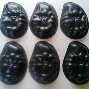 May include: Six black, Santa Claus-shaped molds. Each mold has a detailed face, beard, and hat. The molds are made of a dark, glossy material and are arranged in two rows of three.
