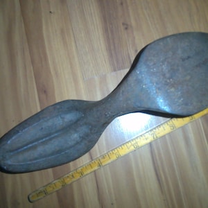 May include: A vintage metal shoe last, a tool used by shoemakers to shape and form shoes. The last is made of cast iron and has a dark gray finish. It is approximately 15 inches long.