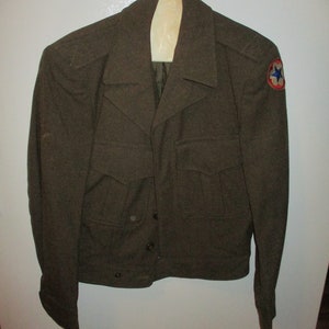 May include: A green military jacket with a star patch on the right shoulder. The jacket has a button closure and two pockets on the front.