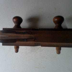 May include: A wooden hand plane with two wooden knobs on either end. The plane has a series of grooves on the top and a metal blade.