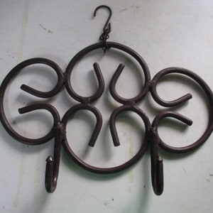 May include: A decorative, dark brown metal wall hook with a unique, swirling design. The hook features a series of curved shapes and two lower hooks for hanging items. A small chain and hook are at the top for easy mounting.