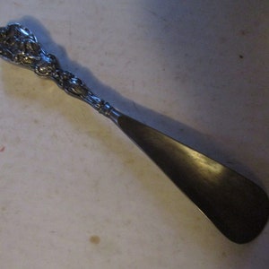 May include: A silver shoehorn with an ornate, floral design on the handle.