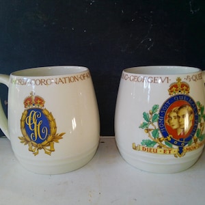 May include: Two white ceramic mugs with handles. One mug features a royal crest with the text "1937 CORONATION OF" and a gold crown. The other mug has a portrait and the text "KING GEORGE VI & QUEEN".