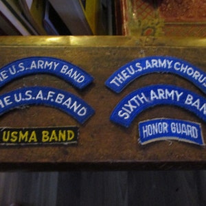 May include: Six blue and white embroidered patches with the text "The U.S. Army Band", "The U.S.A.F. Band", "The U.S. Army Chorus", "Sixth Army Band", "USMA Band", and "Honor Guard".