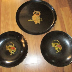 May include: A set of three black serving trays and plates. The large tray features an owl design, while the smaller plates have a mushroom design. The owl and mushroom designs are in yellow and red.