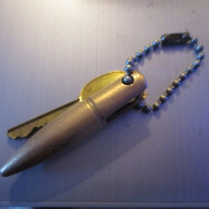 May include: A gold-colored bullet-shaped keychain with a key attached and a silver chain.