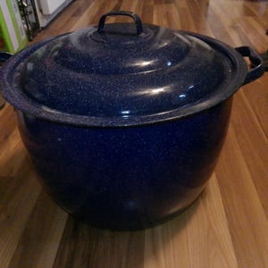 May include: A large, navy blue enamelware pot with a matching lid. The pot has two side handles and a handle on the lid. The speckled finish gives it a vintage look. This cooking pot is suitable for various kitchen uses.