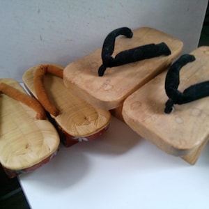 May include: Three pairs of wooden Japanese sandals, or geta, with black fabric straps. The sandals are made of light brown wood and have a simple design.
