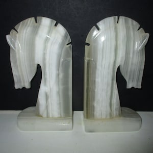 May include: A pair of white marble bookends shaped like horse heads. The bookends have a white and gray striped pattern.
