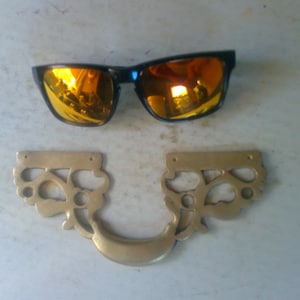 May include: A pair of black sunglasses with orange mirrored lenses and a brass decorative handle with a floral design.