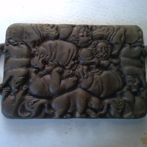 May include: A cast iron serving tray with a raised design of various animals, including hippos and lions. The tray has two handles on the sides.
