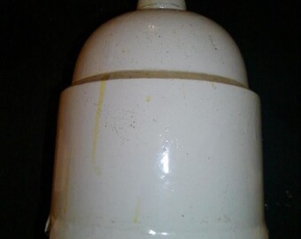 May include: A white ceramic jar with a rounded top and a cylindrical base. The jar has a small, circular lid and a band of darker material around the middle. The surface has a glossy finish and some yellow staining.