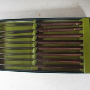 May include: A set of eight stainless steel knives with brown wooden handles and colorful accents. The knives are in a green box.