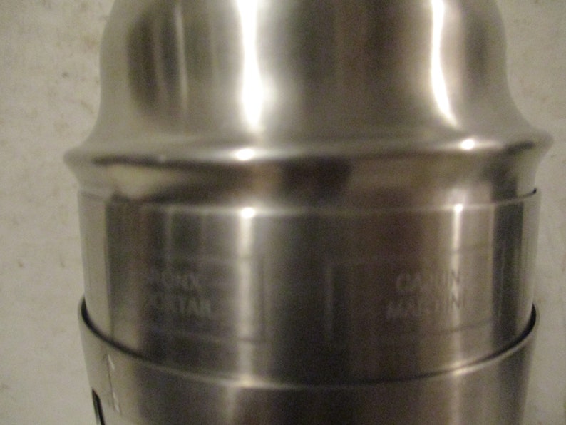 K&ouml;nnte beinhalten: Ein gl&auml;nzender Cocktailshaker aus Edelstahl. Der Shaker hat einen zylindrischen K&ouml;rper mit ausgestelltem Ober- und Unterteil. Die Texte "RIGHT MORTAR" und "CAJUN MACHINE" sind auf der Oberfl&auml;che eingraviert.