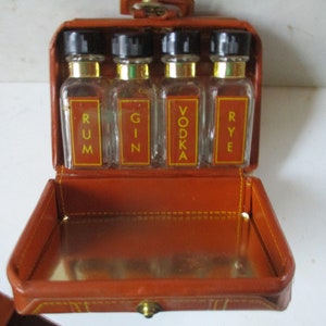 May include: A brown leather travel case with four small glass bottles inside. The bottles are labeled "RUM", "GIN", "VODKA", and "RYE".