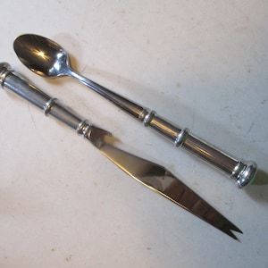 May include: A set of two silver utensils, a spoon and a knife, with decorative handles. The spoon has a rounded bowl and the knife has a pointed tip.