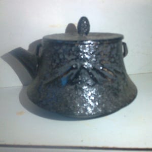 May include: A black ceramic teapot with a textured surface and a small knob on the lid.