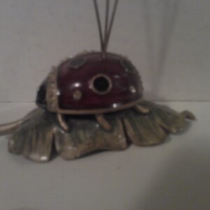 May include: A decorative ladybug figurine with a red body and black spots, perched on a green and gold leaf.