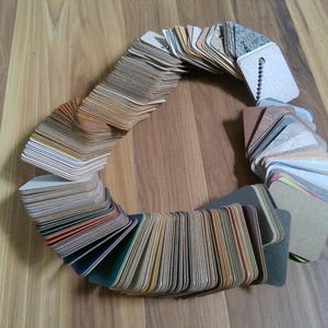 May include: A collection of color swatches arranged in a circular pattern, showcasing a variety of hues and textures. The swatches are made of a thick paper material, with a mix of neutral and vibrant colors. The background is a wooden surface.