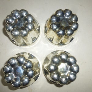 May include: Four silver-colored metal molds for making individual desserts. Each mold has a fluted design with a circular center.